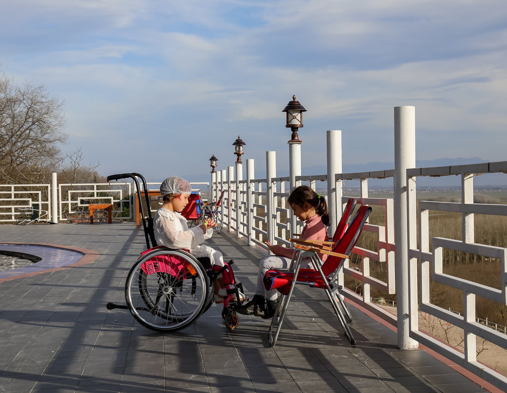 girl resting near metal railing and friend in wheelchair