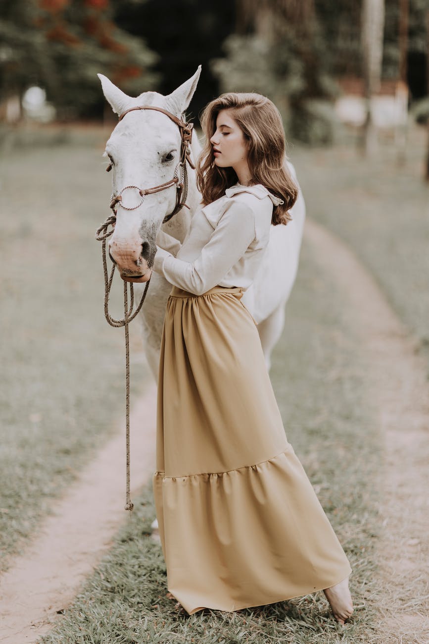 dreamy young lady caressing graceful horse in rural area