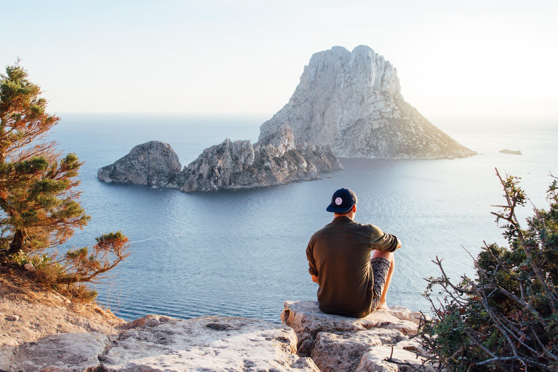 rear view of man sitting on rock by sea