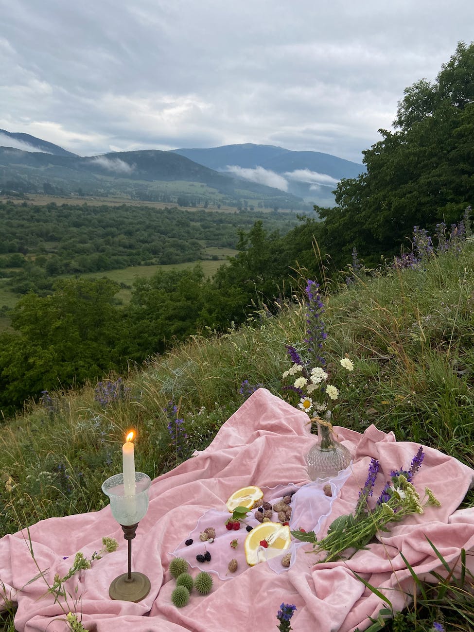 blanket with fruits on grass in mountains